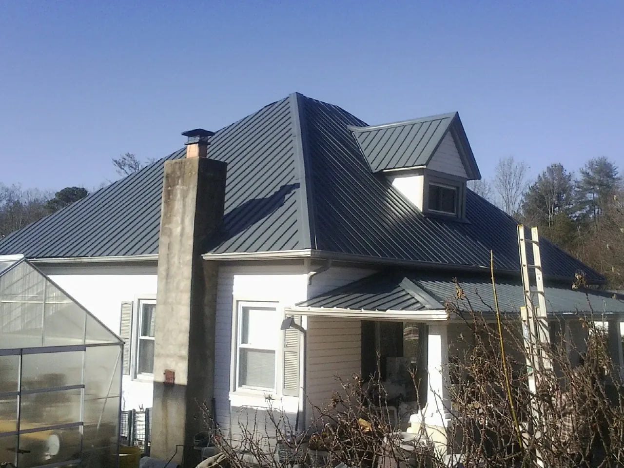 Dark blue standing seam metal roof on a white farmhouse with dormer — Slate & Tile Roof Repair by Roofing Brothers in Elm Grove