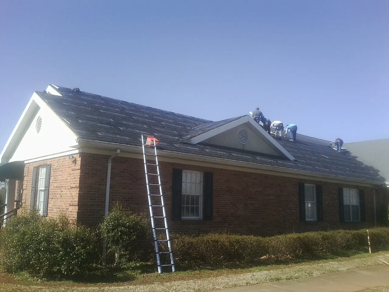 Crew tearing shingles off a brick ranch roof with a ladder set — Emergency Roof Repair work by our crew in Elm Grove
