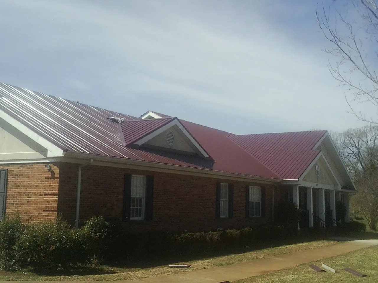 Red metal roof with gabled entries on a long brick building, from a Hail Damage Roof Repair job in Elm Grove