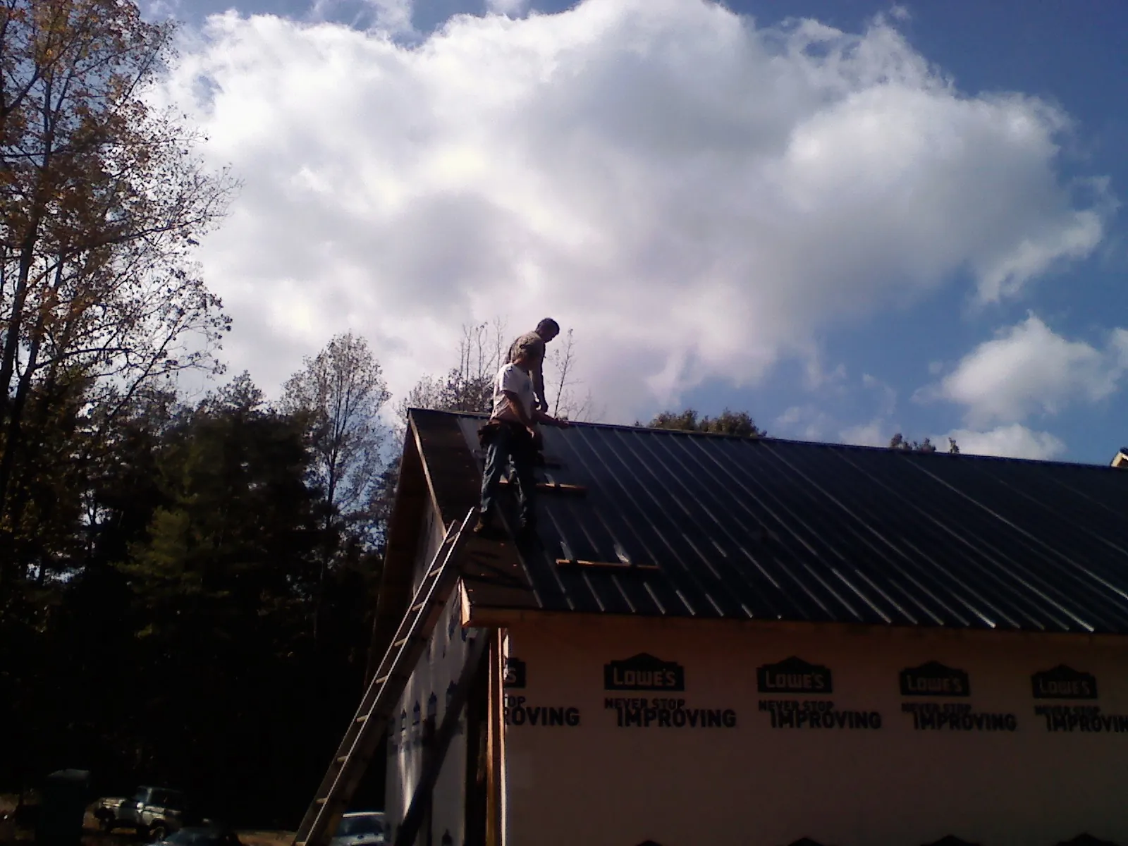 Roofer fastening dark metal panels high against a cloudy sky, from a Roof Inspection job in Elm Grove