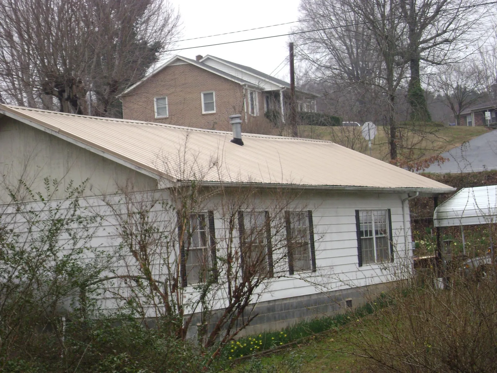 Tan metal roof on a white sided house set into a hillside — Commercial Roofing by Roofing Brothers in Elm Grove