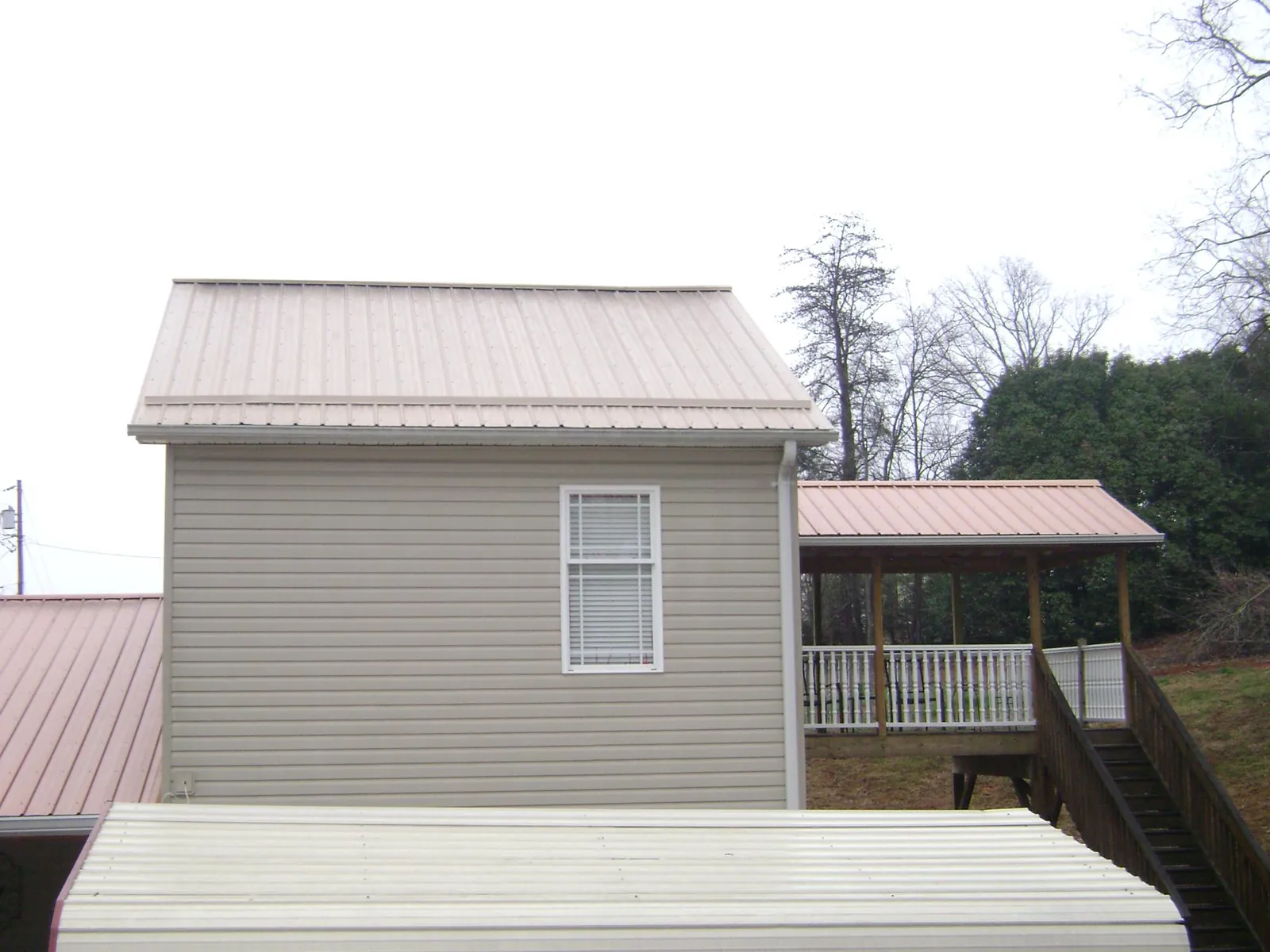 Tan metal roofs on a two story addition and attached porch, from a Roof Replacement job in Elm Grove